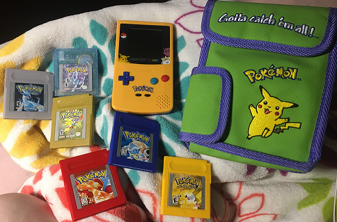 All of the main series Game Boy Pokemon games laid out on a blanket next to a Game Boy Color and vintage carrying bag