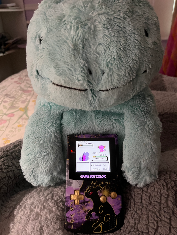 A modded Game Boy Color in front of a large plush Quagsire
